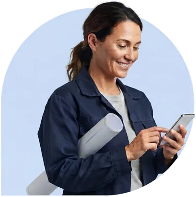 A contractor with rolled plans under her arm, typing on her phone.