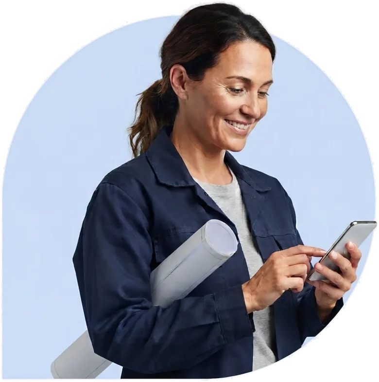 A contractor with rolled plans under her arm, typing on her phone.